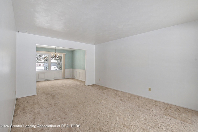 unfurnished room with an inviting chandelier, wainscoting, a decorative wall, and light colored carpet