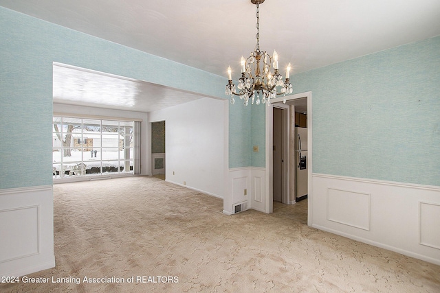 empty room featuring light carpet, wainscoting, a chandelier, and visible vents