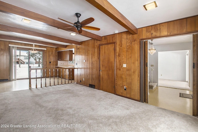 unfurnished living room featuring beam ceiling, light carpet, and wood walls