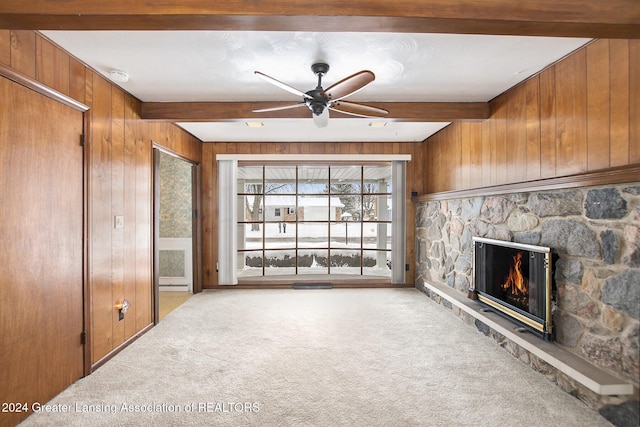 unfurnished living room with beam ceiling, a fireplace, light carpet, wood walls, and ceiling fan