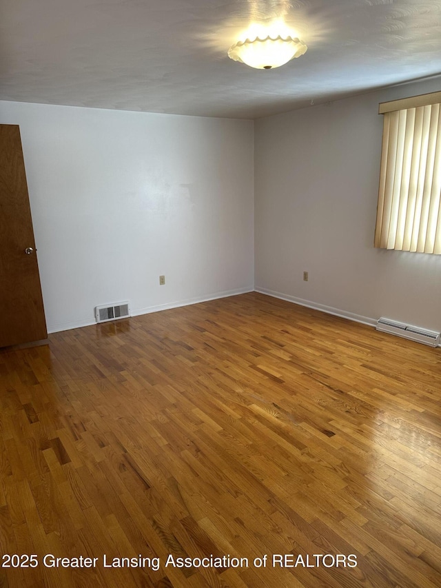 unfurnished room featuring a baseboard heating unit, wood finished floors, visible vents, and baseboards