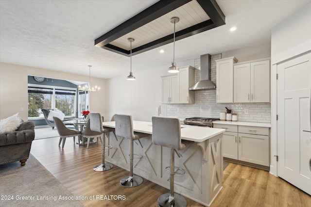 kitchen featuring pendant lighting, a center island, wall chimney range hood, stainless steel gas range, and a breakfast bar area