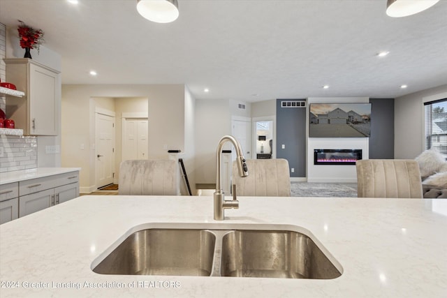 kitchen with backsplash, light stone countertops, and sink