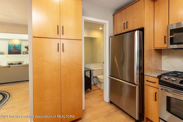 kitchen featuring a fireplace, appliances with stainless steel finishes, backsplash, and light hardwood / wood-style flooring