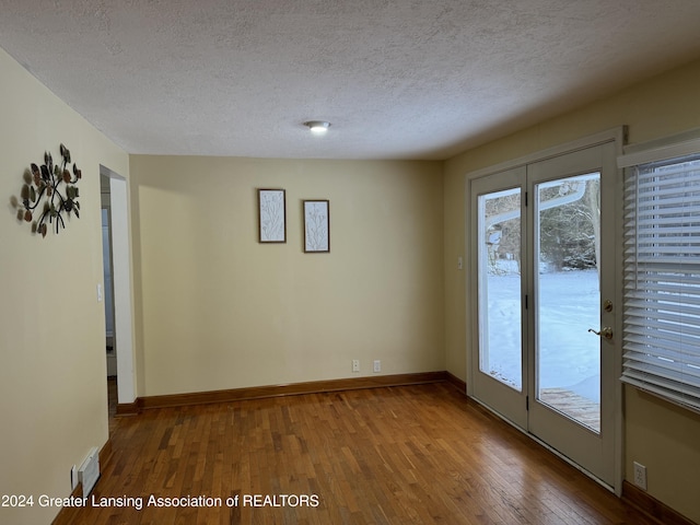 spare room with a textured ceiling, a healthy amount of sunlight, and hardwood / wood-style flooring