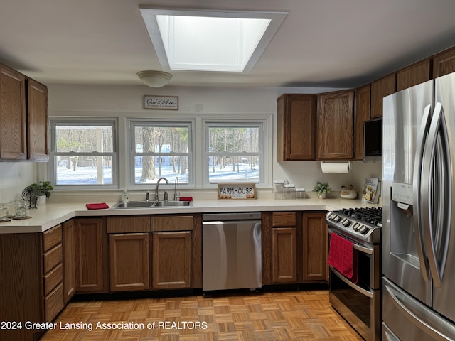 kitchen with sink, a skylight, light parquet floors, and stainless steel appliances