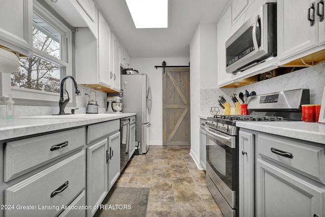 kitchen featuring a barn door, appliances with stainless steel finishes, white cabinets, backsplash, and sink