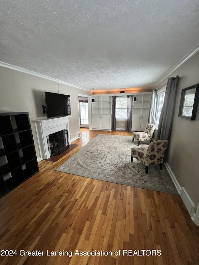 unfurnished living room featuring a textured ceiling, ornamental molding, built in features, and hardwood / wood-style flooring