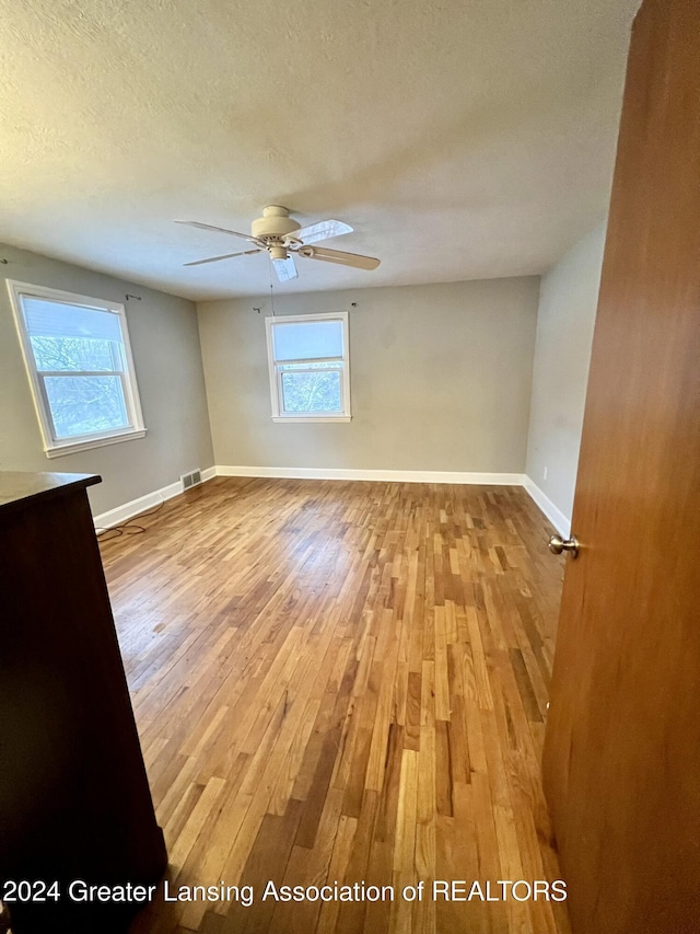 spare room with a textured ceiling, ceiling fan, and light hardwood / wood-style flooring