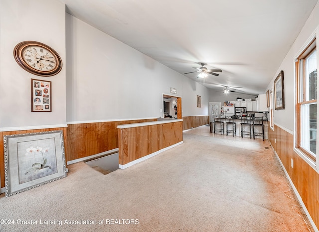 carpeted living room featuring ceiling fan, wood walls, and vaulted ceiling