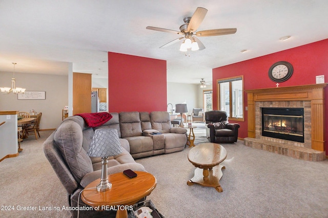 living room with a brick fireplace, ceiling fan with notable chandelier, and carpet flooring