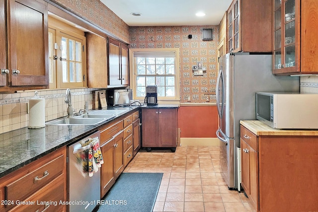 kitchen with appliances with stainless steel finishes, dark stone counters, light tile patterned flooring, and sink