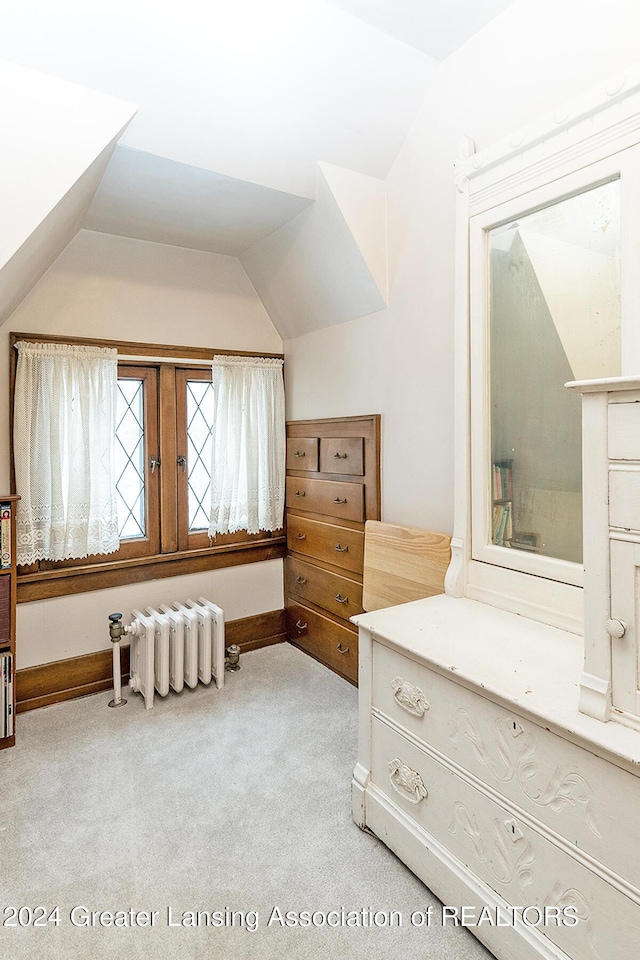 interior space with vaulted ceiling, radiator, and light carpet