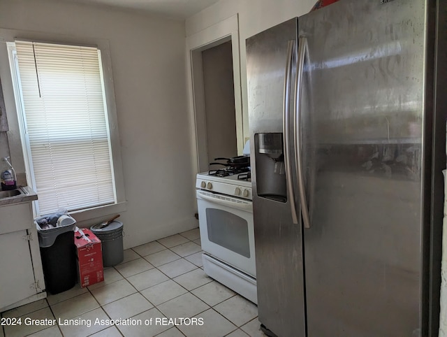 kitchen featuring stainless steel fridge, light tile patterned flooring, and white gas stove