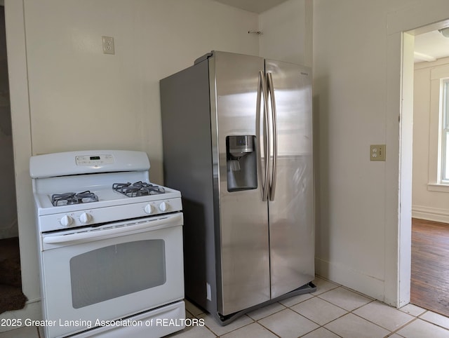 kitchen with light tile patterned floors, white gas range, and stainless steel fridge