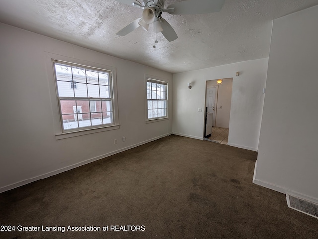 unfurnished room with ceiling fan, dark carpet, and a textured ceiling