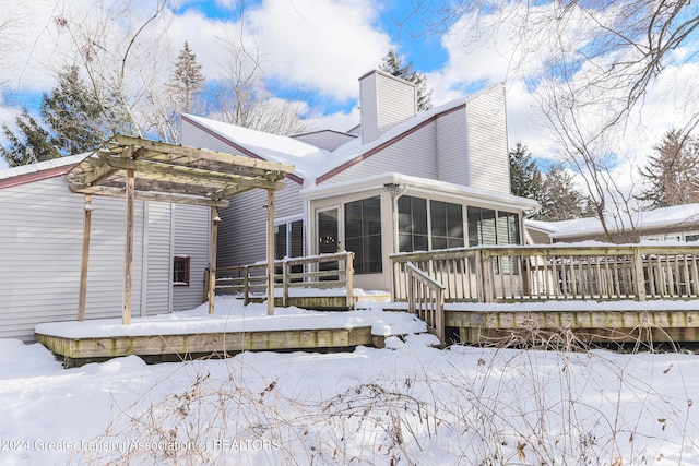 snow covered rear of property featuring a pergola, a wooden deck, and a sunroom