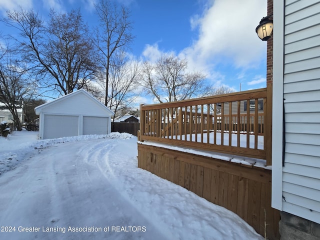 snowy yard with a deck, a garage, and an outbuilding