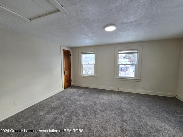 unfurnished room featuring a textured ceiling and dark colored carpet