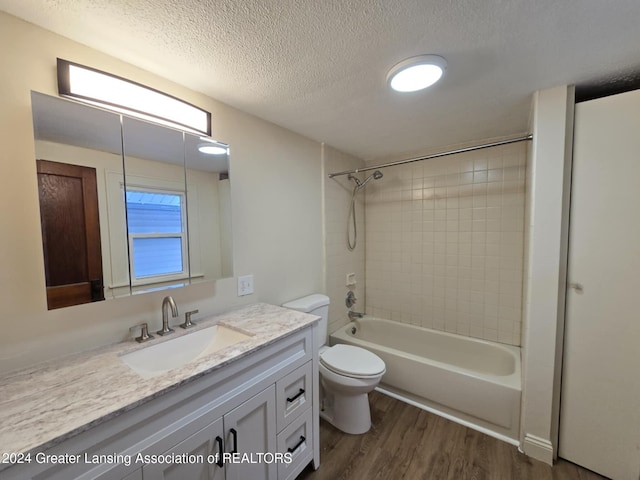 full bathroom featuring toilet, vanity, tiled shower / bath combo, wood-type flooring, and a textured ceiling