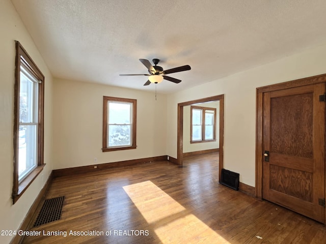 empty room with dark wood-type flooring, plenty of natural light, and ceiling fan