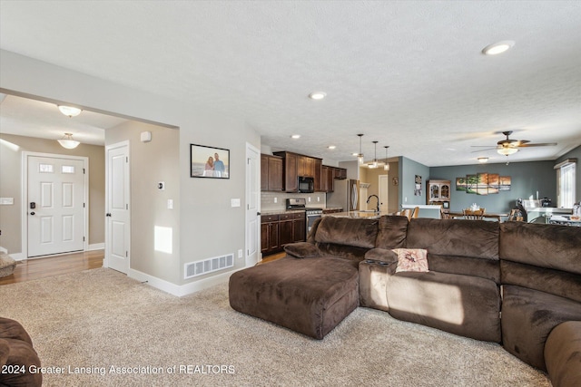 living room featuring ceiling fan, a textured ceiling, and light carpet