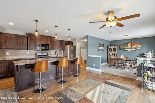 kitchen featuring tasteful backsplash, appliances with stainless steel finishes, a center island with sink, and a breakfast bar