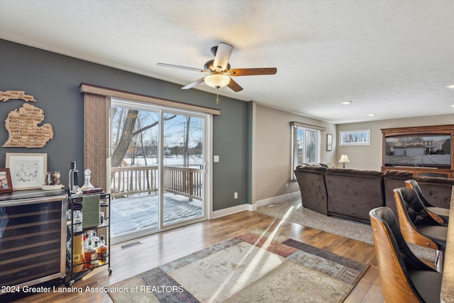 living room with beverage cooler, light wood-type flooring, a textured ceiling, and a healthy amount of sunlight