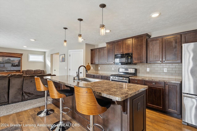 kitchen featuring decorative light fixtures, sink, appliances with stainless steel finishes, and an island with sink