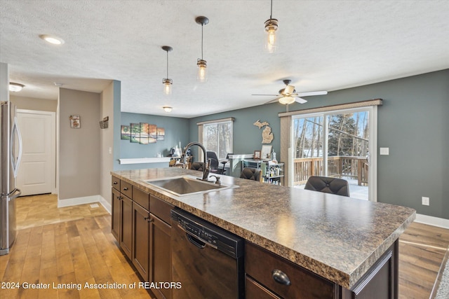 kitchen featuring pendant lighting, sink, black dishwasher, light wood-type flooring, and a kitchen island with sink