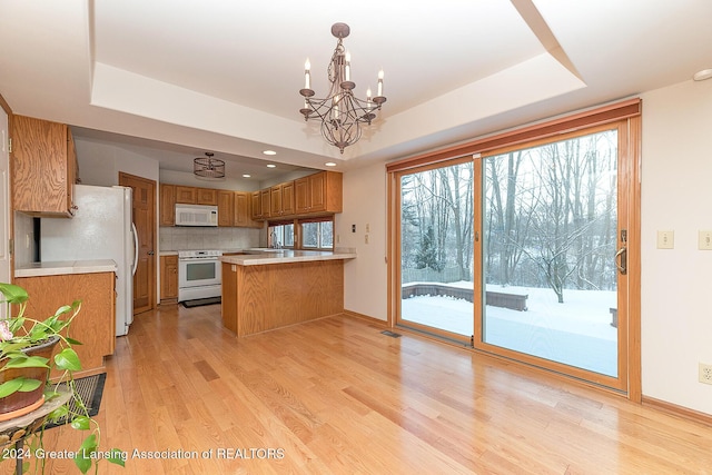 kitchen with white appliances, light hardwood / wood-style flooring, tasteful backsplash, and a tray ceiling