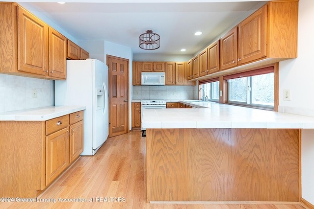 kitchen featuring white appliances, light wood-type flooring, kitchen peninsula, and tasteful backsplash