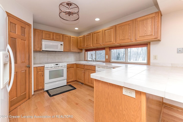 kitchen featuring white appliances, sink, light wood-type flooring, backsplash, and tile countertops