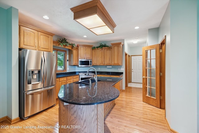 kitchen with appliances with stainless steel finishes, sink, a center island with sink, and light wood-type flooring