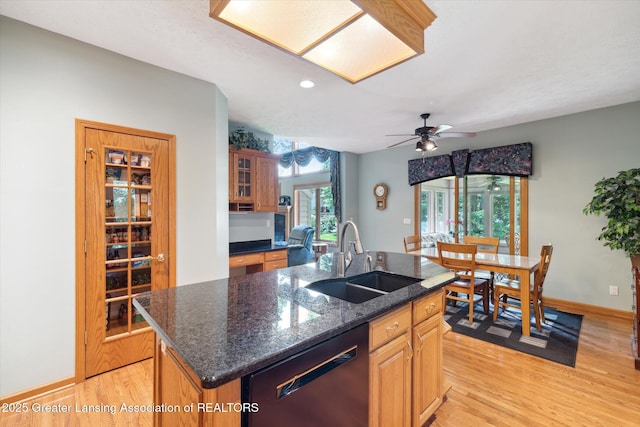 kitchen with dishwasher, sink, dark stone counters, light hardwood / wood-style floors, and a center island with sink