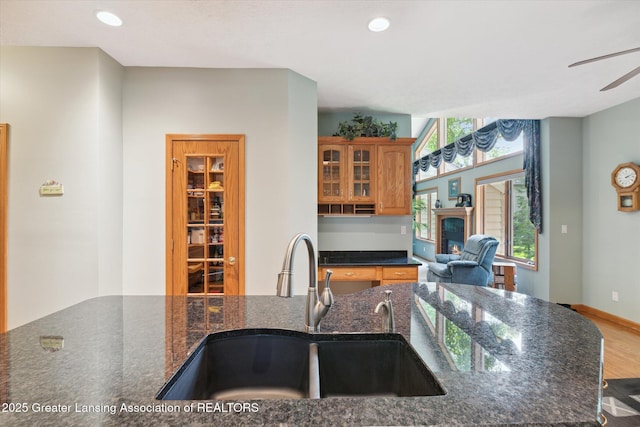 kitchen with sink, a breakfast bar area, wood-type flooring, ceiling fan, and dark stone counters