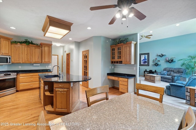 kitchen with sink, built in desk, a center island with sink, stainless steel appliances, and light hardwood / wood-style floors