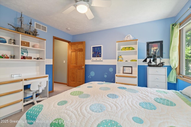 bedroom with built in desk, light colored carpet, a textured ceiling, and ceiling fan