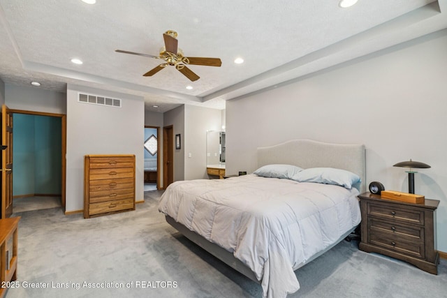 carpeted bedroom featuring a raised ceiling, ceiling fan, a textured ceiling, and ensuite bath