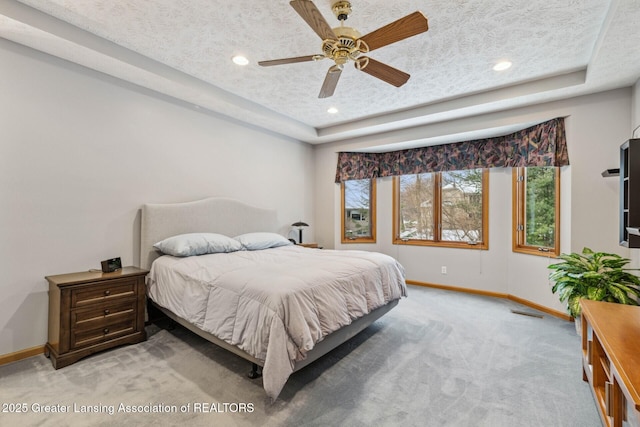 carpeted bedroom featuring ceiling fan, a tray ceiling, and a textured ceiling