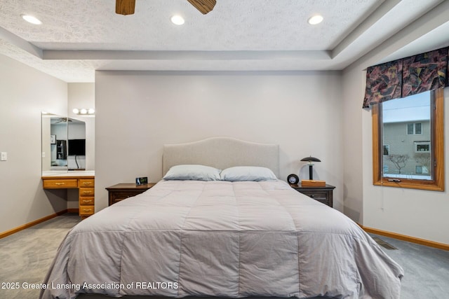 carpeted bedroom with ensuite bath, built in desk, a raised ceiling, and a textured ceiling