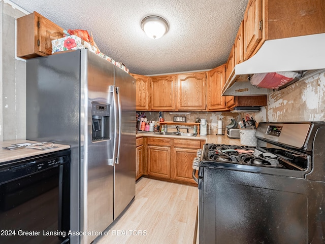 kitchen with black gas range oven, sink, stainless steel fridge, light hardwood / wood-style flooring, and a textured ceiling