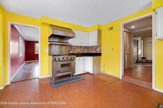 kitchen featuring high end stainless steel range oven, white cabinets, backsplash, and wall chimney range hood