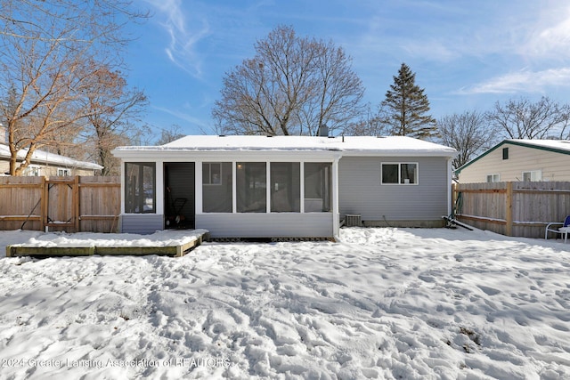 snow covered rear of property featuring a sunroom