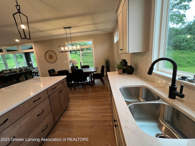 6097 Southridge Rd, East Lansing, MI 48823 - kitchen featuring wood finished floors, hanging light fixtures, backsplash, light stone countertops, and a chandelier