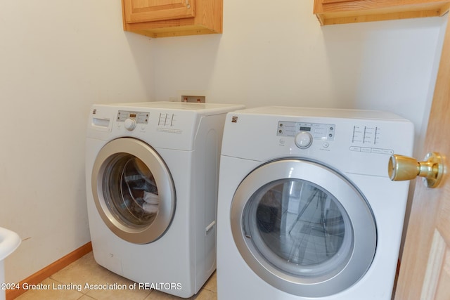 laundry room featuring washing machine and dryer, light tile patterned floors, and cabinets