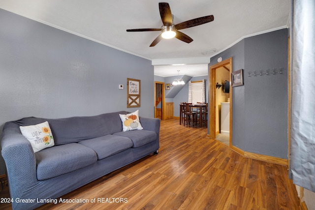 living room featuring hardwood / wood-style flooring, ceiling fan with notable chandelier, and ornamental molding