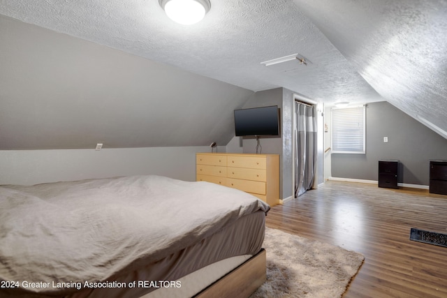 bedroom featuring hardwood / wood-style flooring, a textured ceiling, and vaulted ceiling