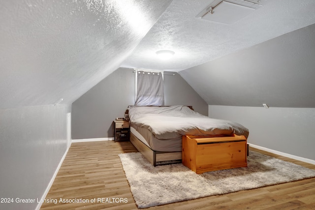 bedroom with wood-type flooring, lofted ceiling, and a textured ceiling