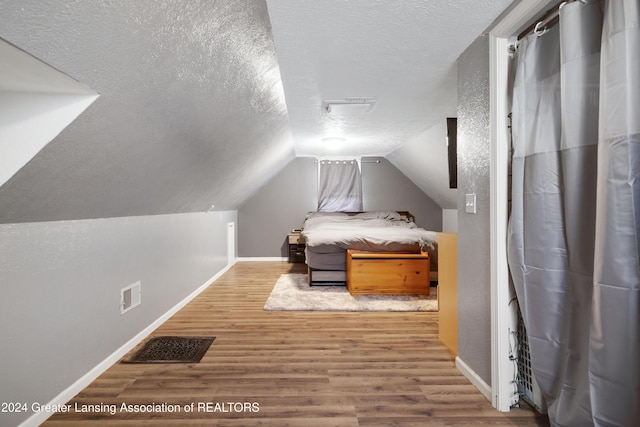 bedroom featuring hardwood / wood-style floors, a textured ceiling, and lofted ceiling